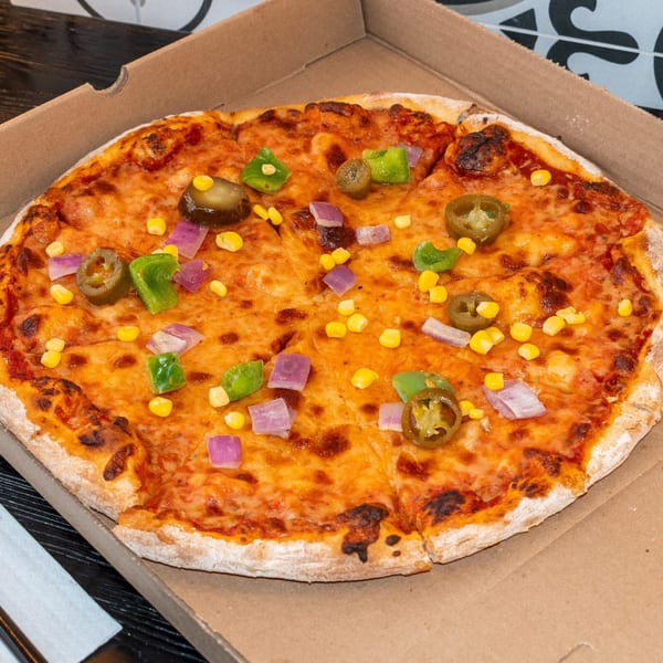 A Bombay Baking Co. pizza with cheese, corn, green peppers, red onions, and jalapeños in a box.