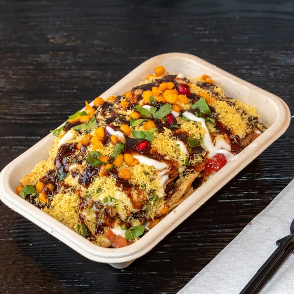 Bombay Baking Co.'s savory chaat, topped with sauces, crunchy sev, and fresh herbs in a takeout container.