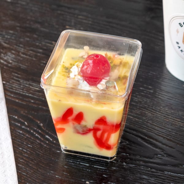 Bombay Baking Co. dessert cup with yellow pudding, red swirls, whipped cream, and a cherry.