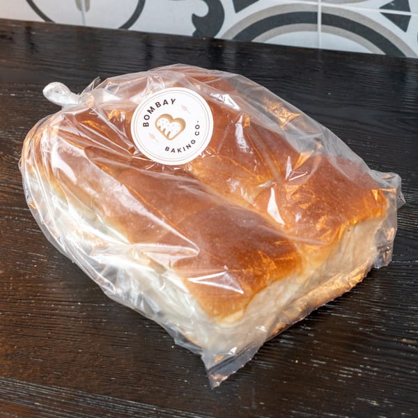 A clear plastic bag of Bombay Baking Co. dinner rolls sits on a dark wooden surface.