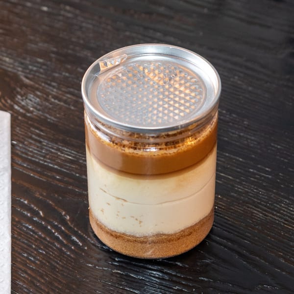 Layered dessert in a clear jar with a silver pull-tab lid, on a dark wooden surface.