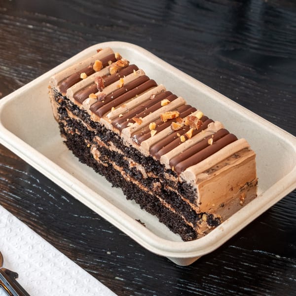 A rectangular slice of chocolate cake with layers of frosting and chocolate bars, topped with nuts.
