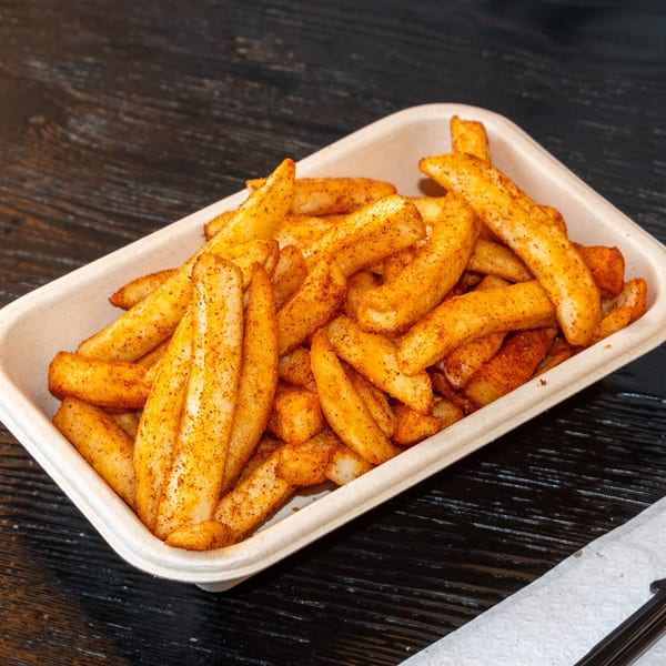 Seasoned french fries in a light brown rectangular container on a dark wooden table.