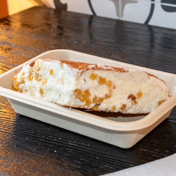 A dessert in a light brown container, topped with white cream and golden fruit pieces.