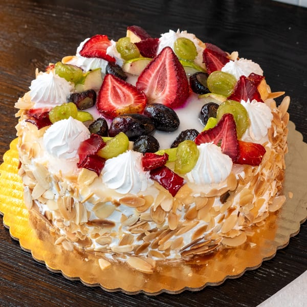 A round cake with whipped cream, strawberries, green grapes, and dark berries, topped with almond flakes.