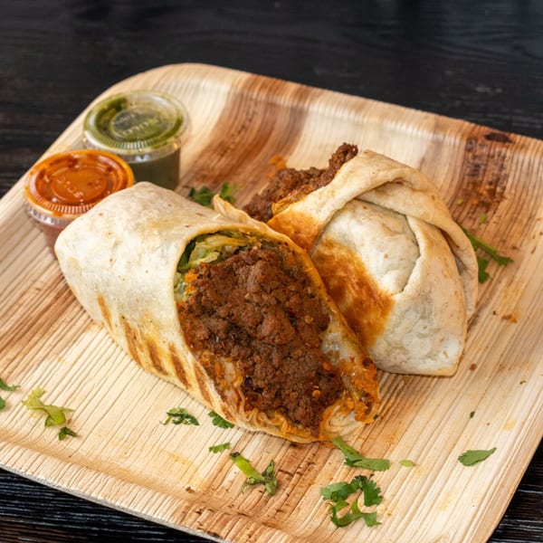 Two Bombay Baking Co. burritos with meat and lettuce, served with green and orange sauces.