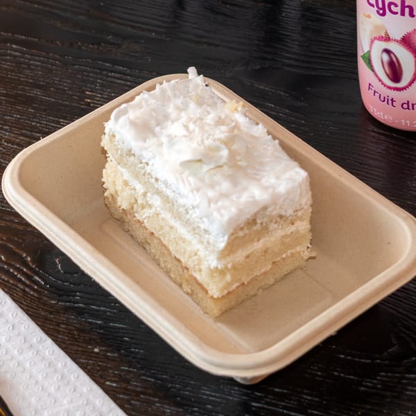 A slice of Bombay Baking Co.'s coconut cake with white frosting on a beige tray.