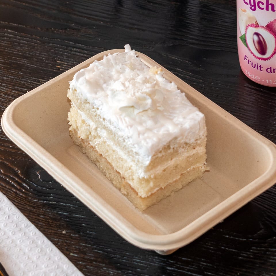 A slice of Bombay Baking Co.'s coconut cake with white frosting on a beige tray.