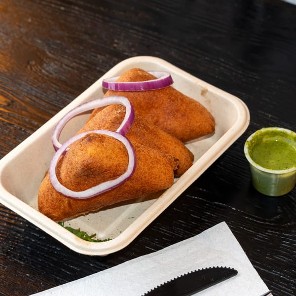 Three golden-brown fried pastries with red onion rings, served with green chutney on a dark wooden table.