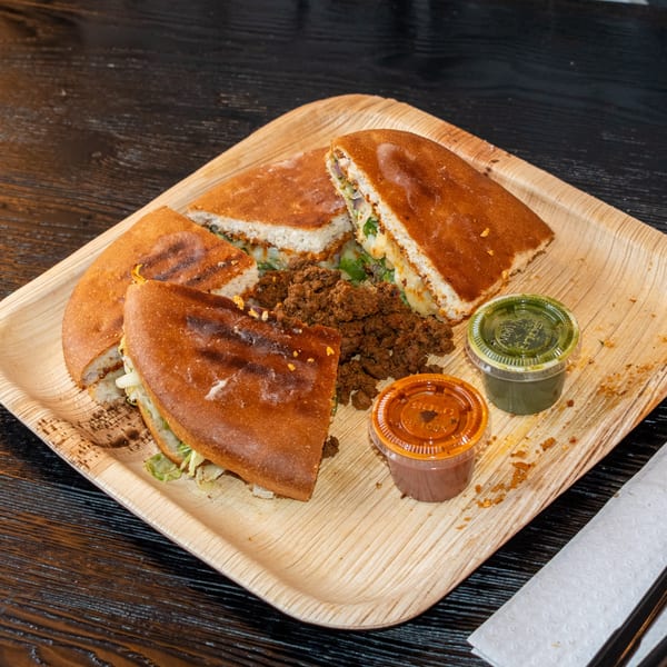 Bombay Baking Co. sandwiches with meat, lettuce, and sauces on a wooden tray.