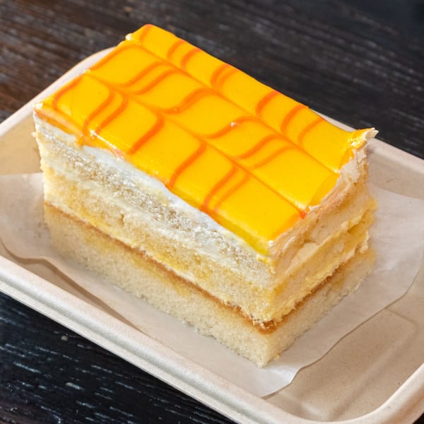 A rectangular slice of cake with yellow and orange striped icing, and layered with cream.