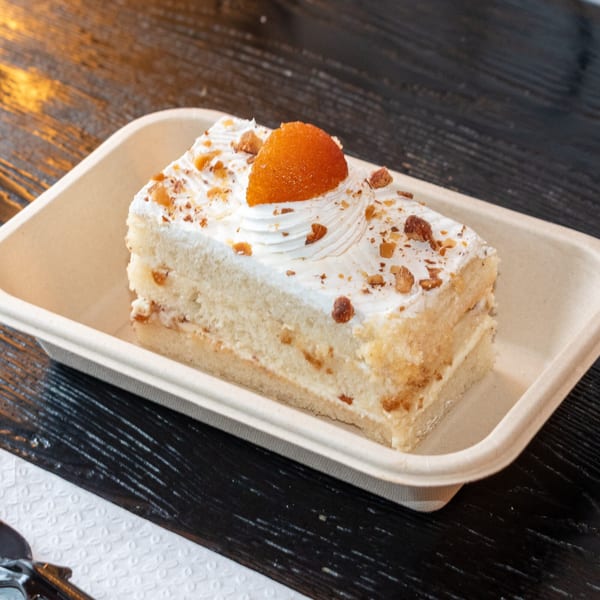 A slice of Bombay Baking Co.'s white cake with cream, nuts, and an orange jelly topping.