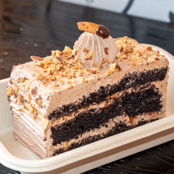 A slice of chocolate cake with light brown frosting, topped with nuts and an almond.