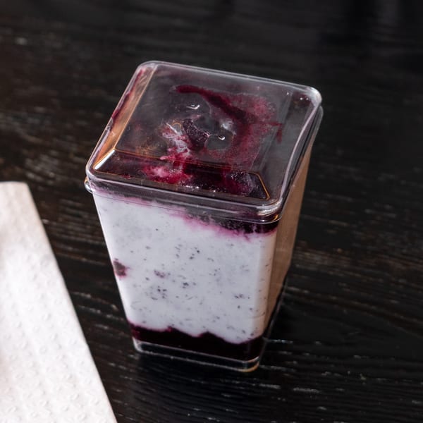 A clear plastic container of blueberry yogurt parfait with a dark berry swirl on a wooden table.