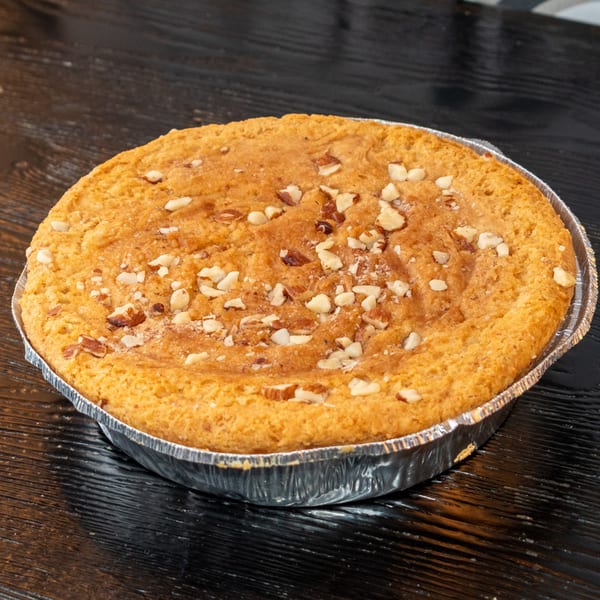 Round baked good with chopped nuts on top, in a foil pan on a dark wooden surface.