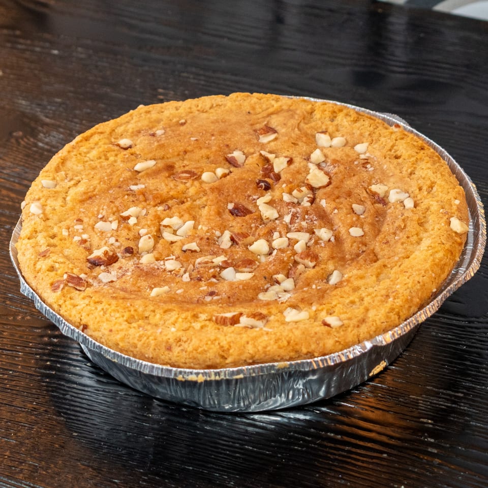 Round baked good with chopped nuts on top, in a foil pan on a dark wooden surface.