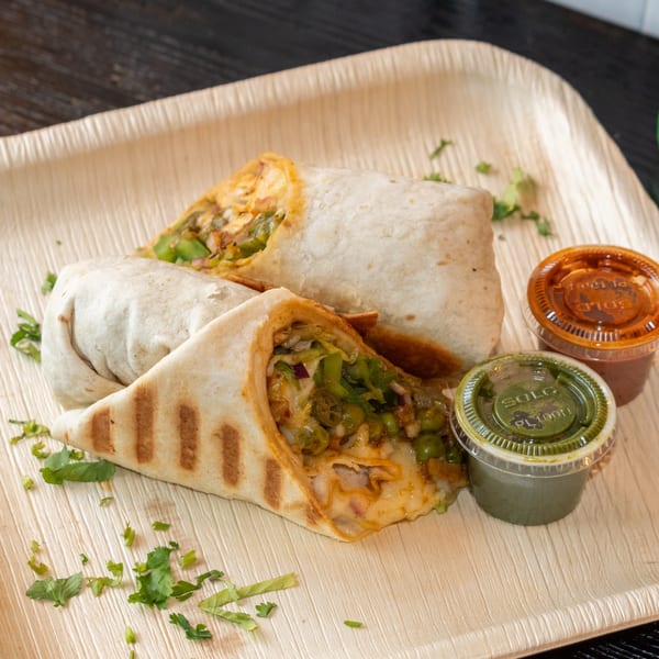 Two Bombay Baking Co. burritos with green and red sauces on a wooden platter.