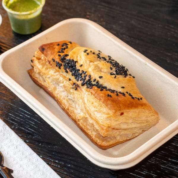 Golden brown puff pastry, topped with black sesame seeds, in a light brown tray.