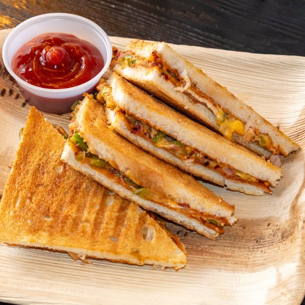 Grilled sandwiches with savory filling and a side of ketchup on a wooden plate from Bombay Baking Co.