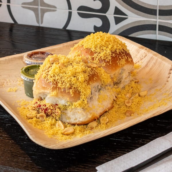 Two Bombay Baking Co. pav buns topped with sev and peanuts, served with two sauces.