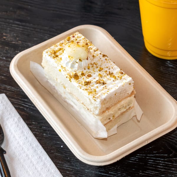 A slice of Bombay Baking Co.'s white cake with pistachio crumbs and a cream dollop.
