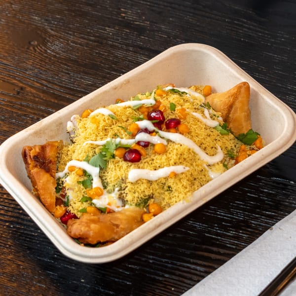 Bombay Baking Co.'s samosa chaat, topped with sev, pomegranate, and yogurt sauce in a to-go container.
