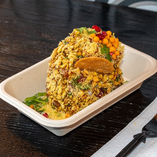 Bombay Baking Co.'s bhel puri, a savory Indian snack, in a disposable container on a dark table.