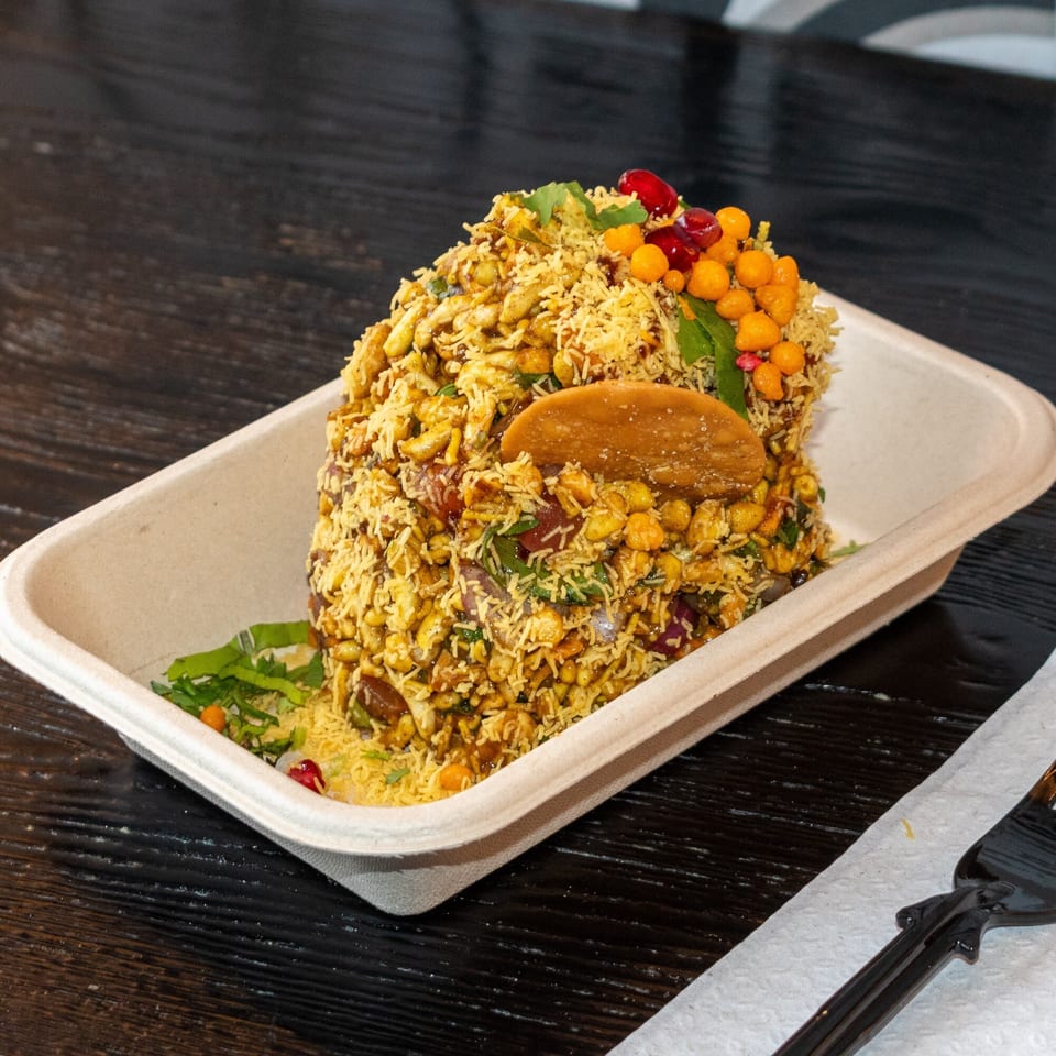 Bombay Baking Co.'s bhel puri, a savory Indian snack, in a disposable container on a dark table.
