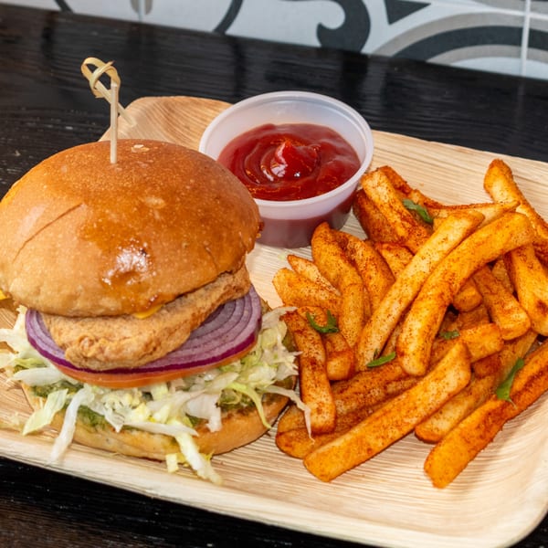 A chicken burger with lettuce, tomato, and onion, served with seasoned fries and ketchup on a wooden tray.