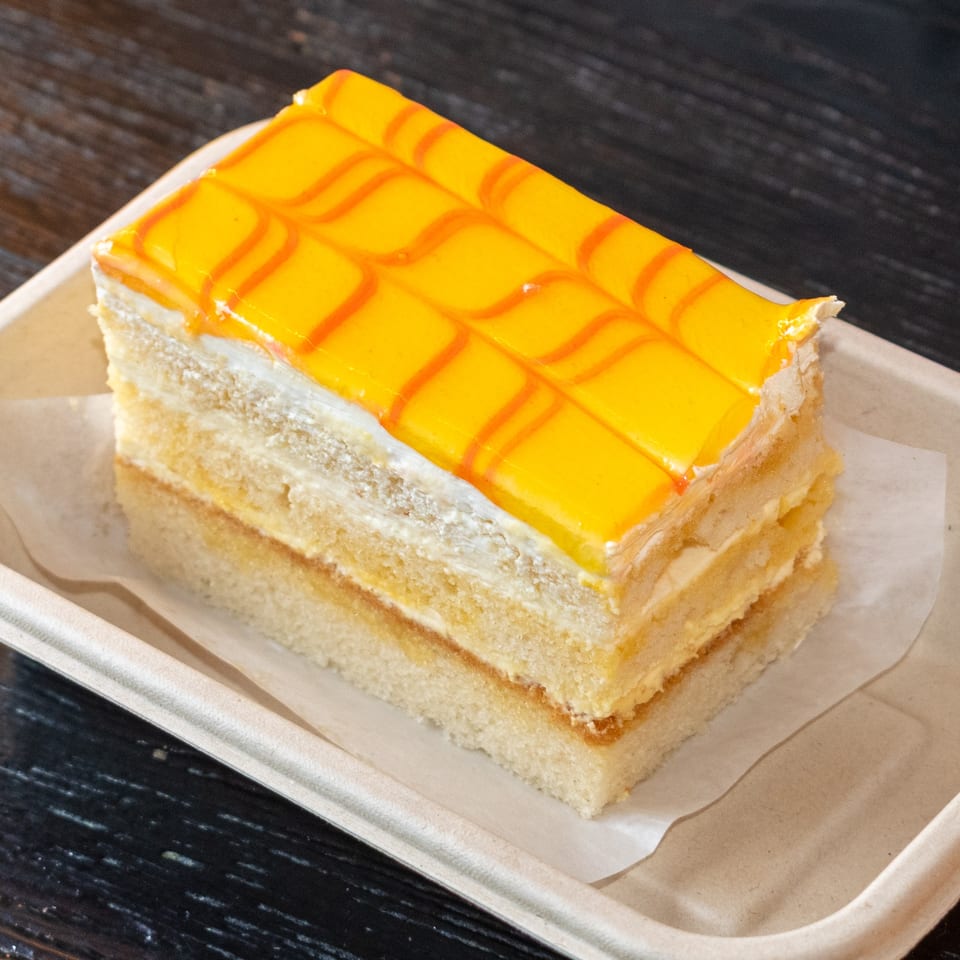 A rectangular slice of cake with yellow and orange striped icing, served in a light brown container.