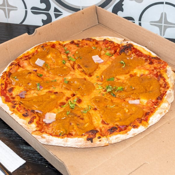 A Bombay Baking Co. pizza with orange sauce, red onion, and cilantro in a cardboard box.