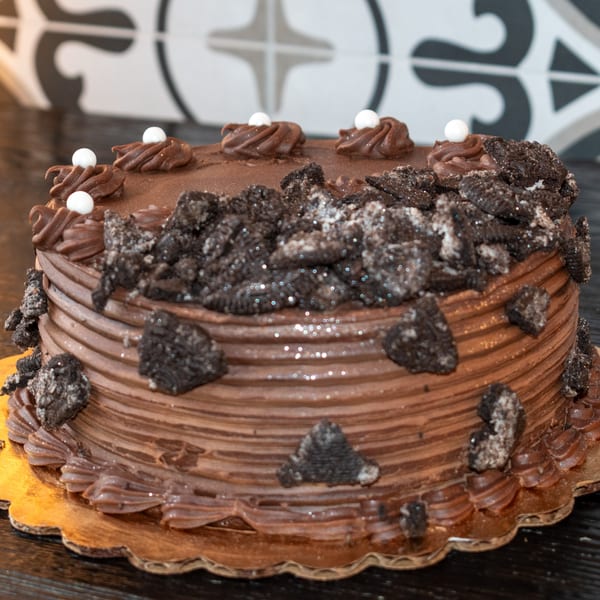 A chocolate cake with chocolate frosting, topped with crushed cookies and white candy pearls.