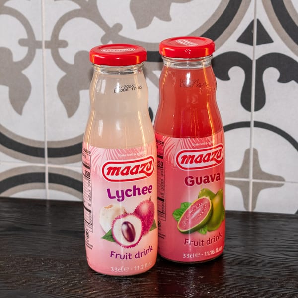 Two Maaza fruit drinks, lychee and guava flavors, on a dark surface with patterned tiles.