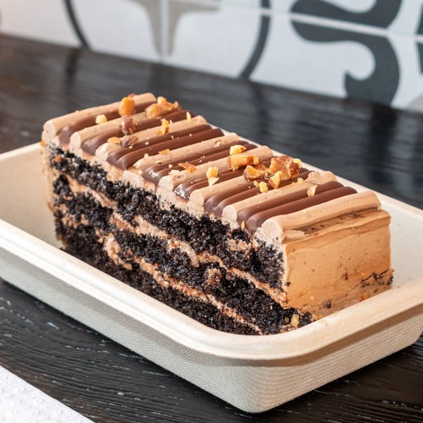 A rectangular slice of chocolate cake with layers of cream, topped with chocolate frosting and nuts.