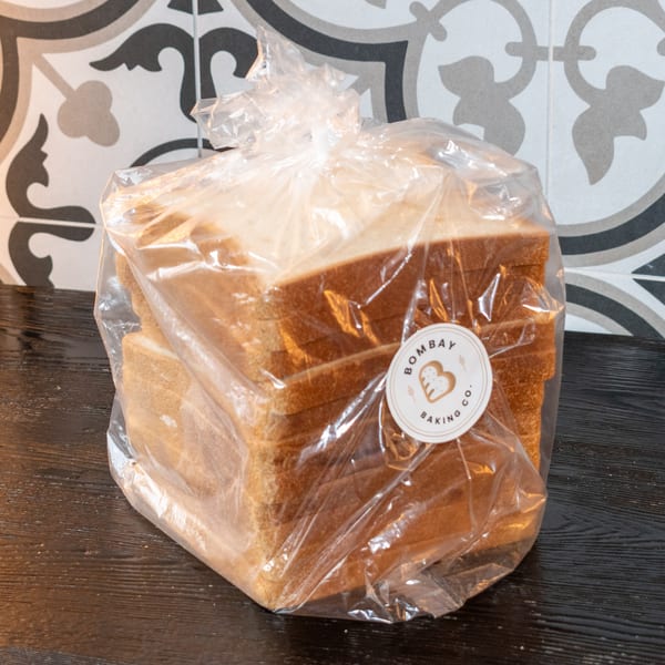 Sliced bread in a plastic bag with a "Bombay Baking Co." label on a dark wooden surface.
