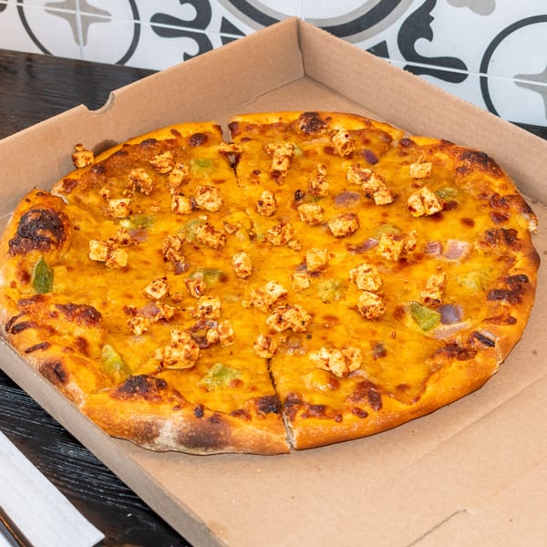 A Bombay Baking Co. paneer tikka pizza with green peppers and onions in a cardboard box.