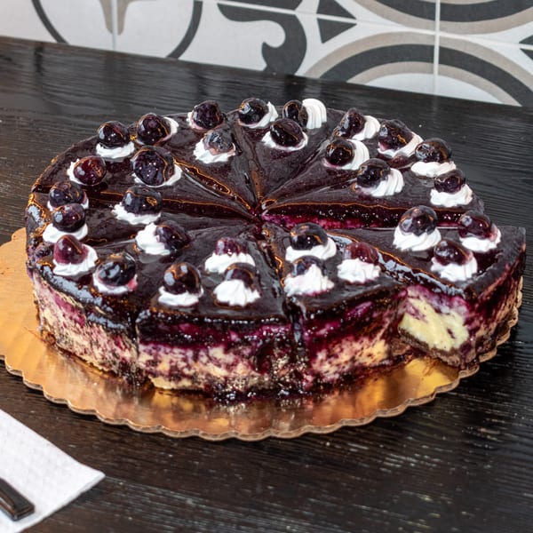 Sliced blueberry cheesecake with whipped cream and whole blueberries on a gold platter.
