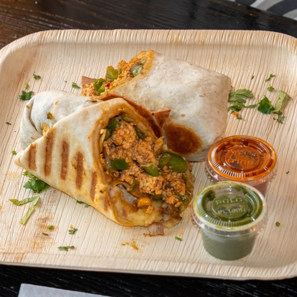 Two Bombay Baking Co. burritos with green peppers and sauces on a wooden tray.