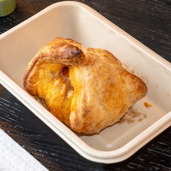 Golden-brown pastry in a light brown paper container on a dark wooden table.