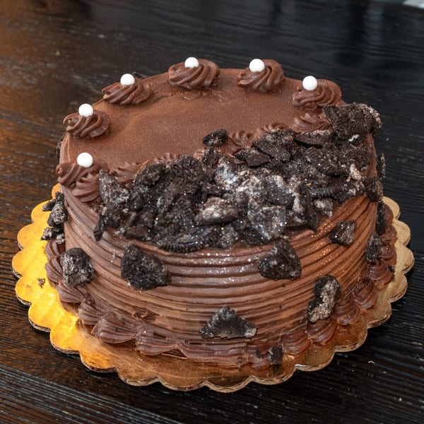 A chocolate cake with cookie crumbles, white pearls, and glitter on a gold scalloped base.
