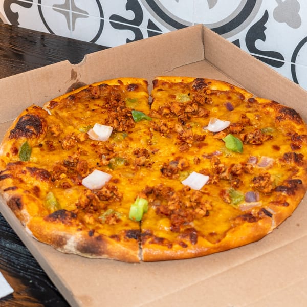 A Bombay Baking Co. pizza with chicken, green peppers, and onions in a cardboard box.