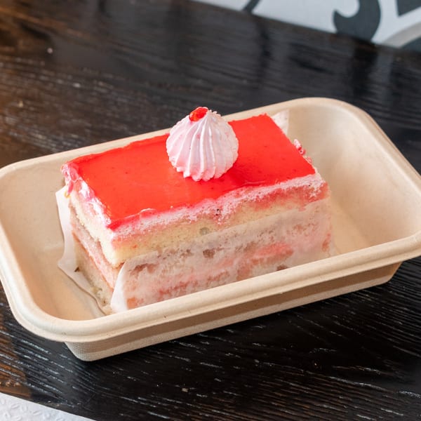 A slice of Bombay Baking Co.'s strawberry cake with red glaze and a dollop of cream.