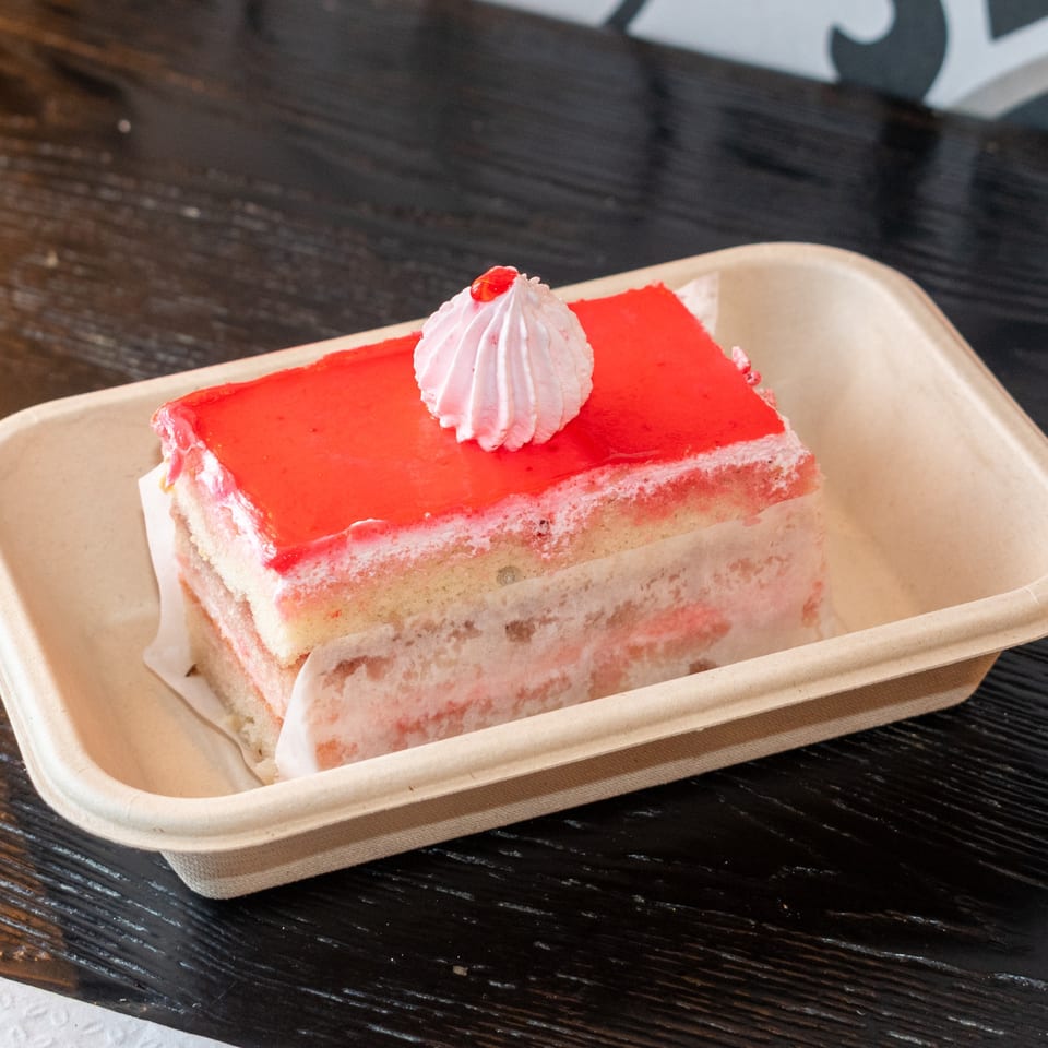 A slice of Bombay Baking Co.'s strawberry cake with red glaze and a dollop of cream.