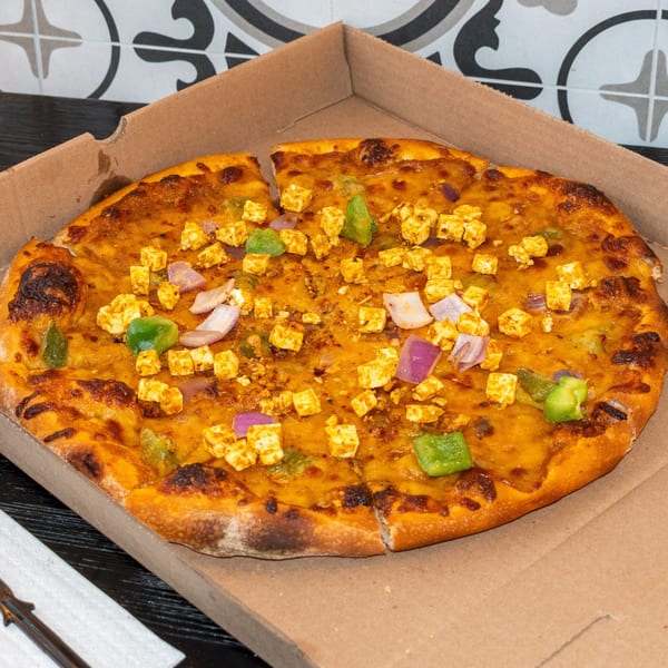 Bombay Baking Co. paneer pizza with green peppers and red onions in a cardboard box.