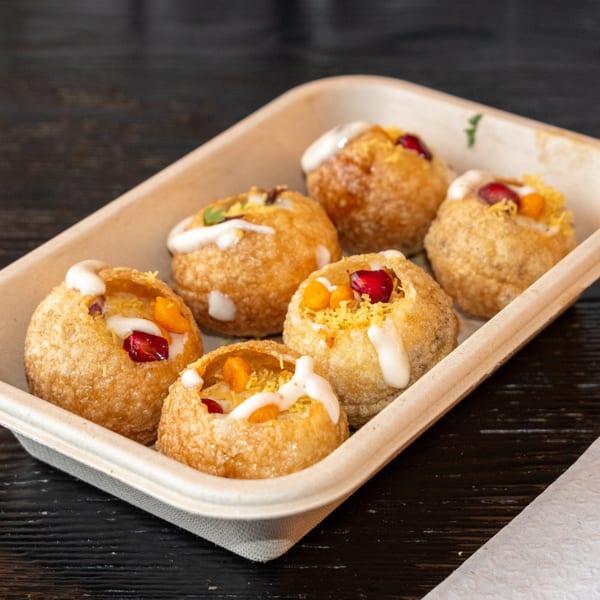 Six golden-fried pani puri shells filled with colorful toppings and drizzled with white sauce in a tray.