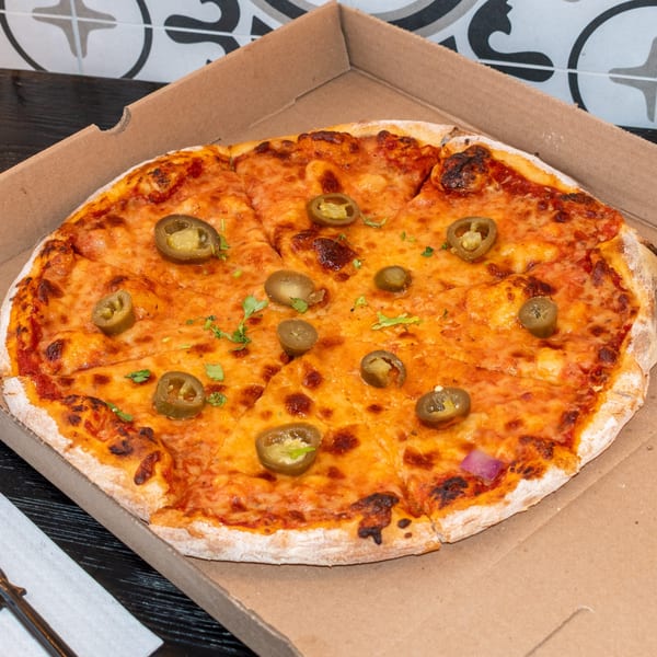 A freshly baked pizza with melted cheese, jalapeños, and cilantro in a cardboard box.