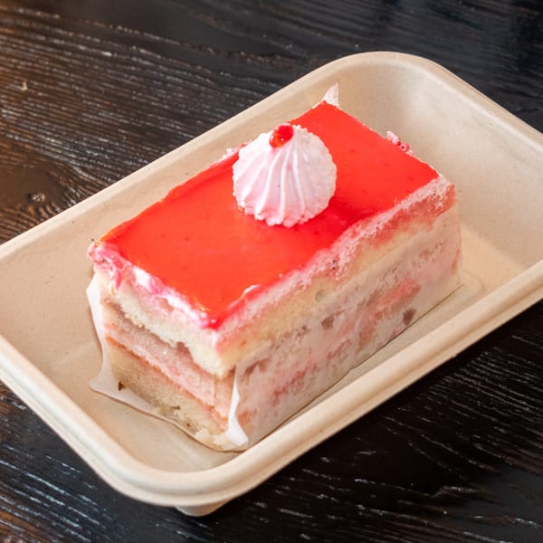 A slice of strawberry cake with white frosting and a dollop of whipped cream on a brown tray.