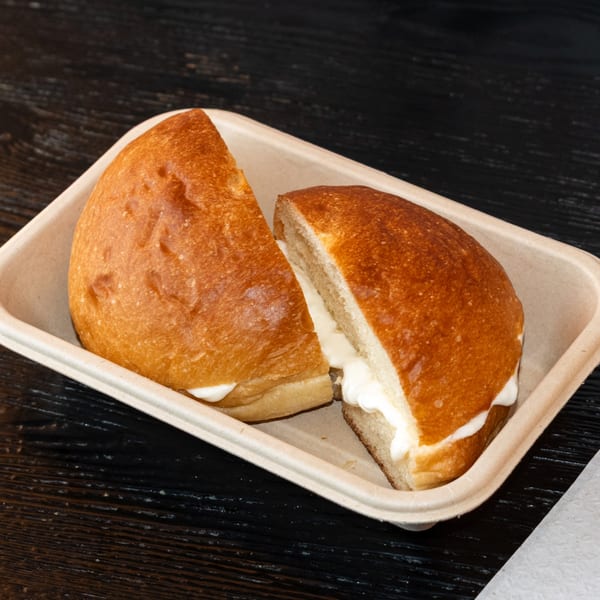 Two halves of a Bombay Baking Co. sweet bun filled with cream, in a takeout container.
