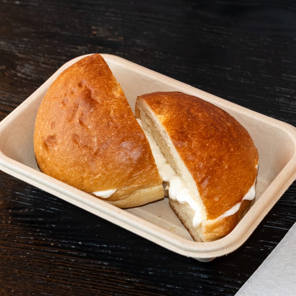 Two halves of a Bombay Baking Co. sweet bun filled with cream, in a takeout container.